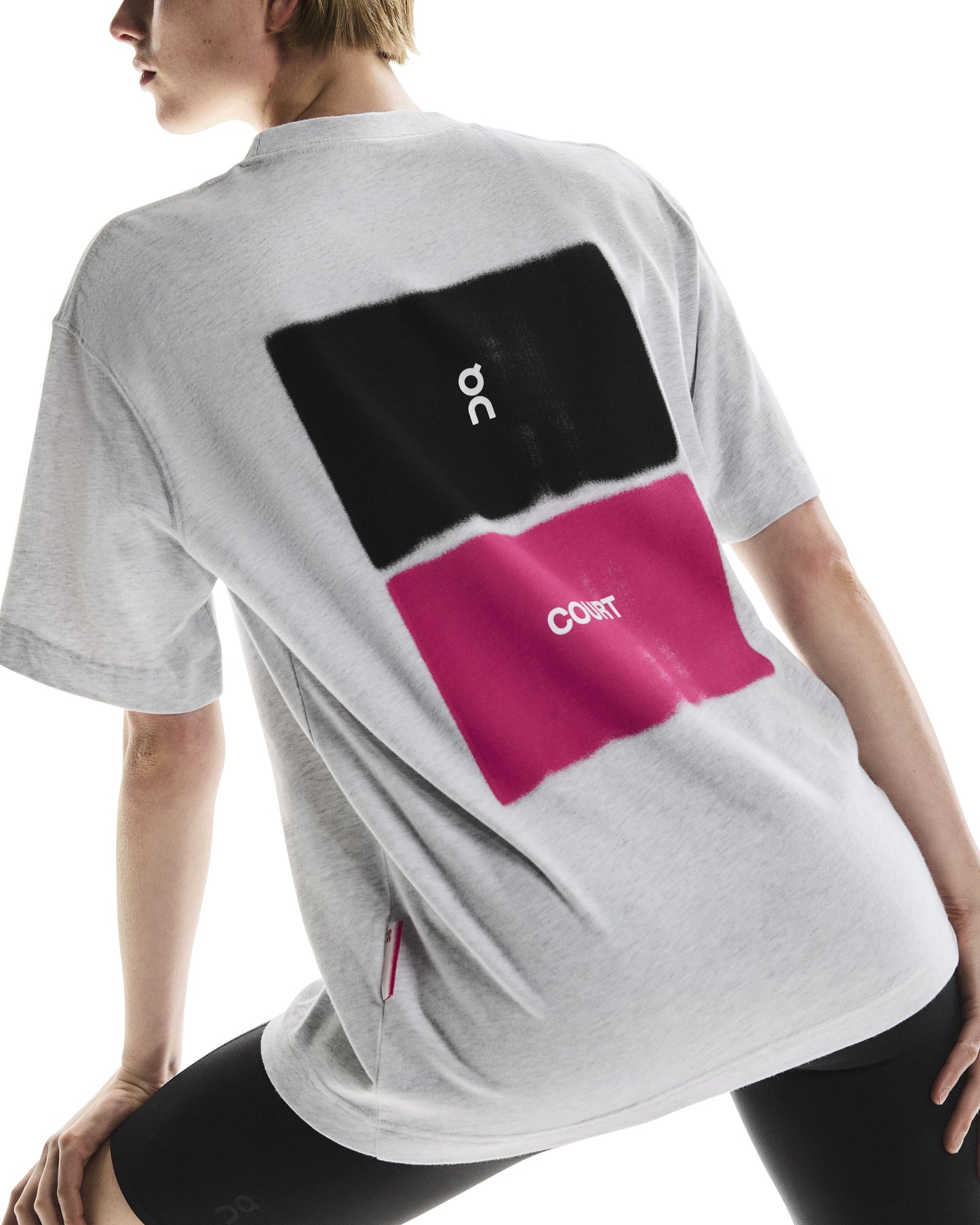 Back of person wearing a grey t-shirt with black and pink On Court design on the back